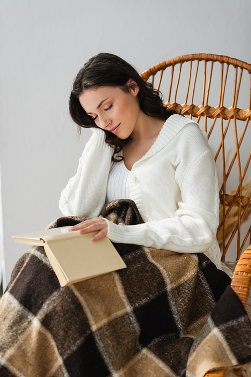 young woman with book sleeping in wicker chair under checkered blanket