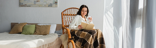 smiling woman reading book while resting in wicker chair with cup of tea, banner