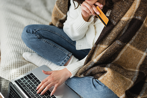 cropped view of woman with credit card typing on laptop on bed