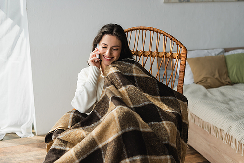 happy woman sitting in wicker chair with closed eyes and talking on mobile phone