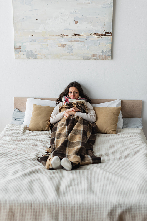 full length view of frozen woman in warm socks lying in bed under plaid blanket