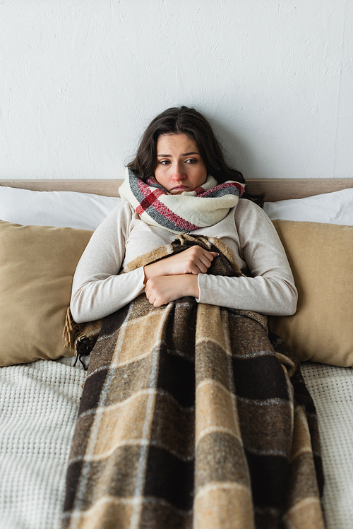 sick and upset woman looking away while lying in bed under checkered blanket