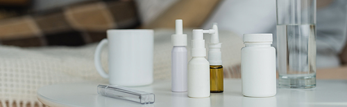 spray bottles and containers with medication near thermometer and drinks on white table, banner