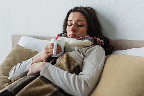 diseased woman lying under checkered blanket with cup of tea