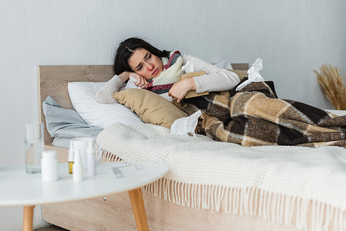 ill woman lying in bed under checkered blanket with pack of paper napkins