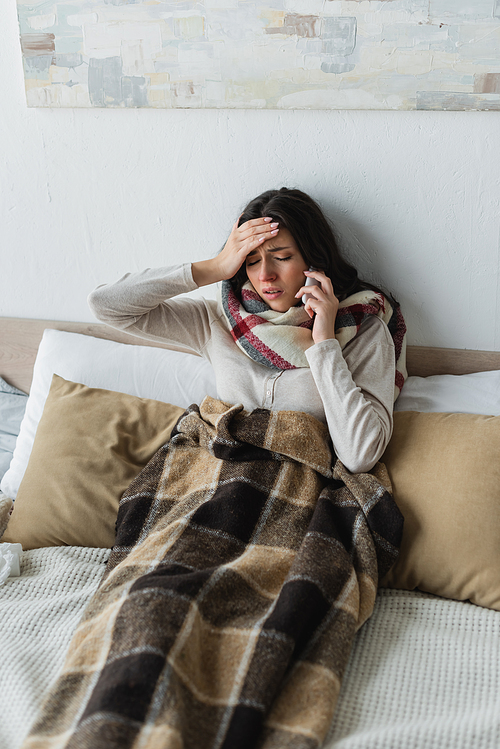 sick woman with closed eyes talking on smartphone while suffering from headache in bed