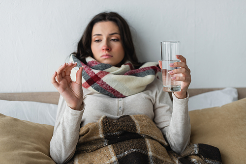 diseased and sad woman lying in bed with glass of water and looking at pill