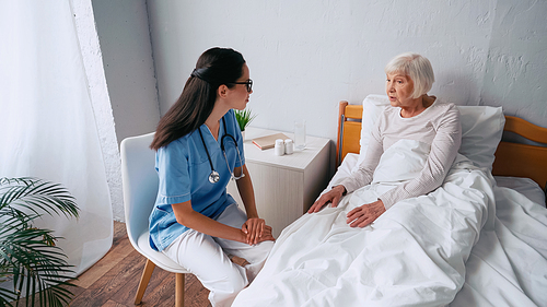 young nurse in eyeglasses and aged woman talking in clinic