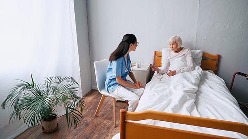 Geriatrician nurse in eyeglasses and senior woman talking in clinic