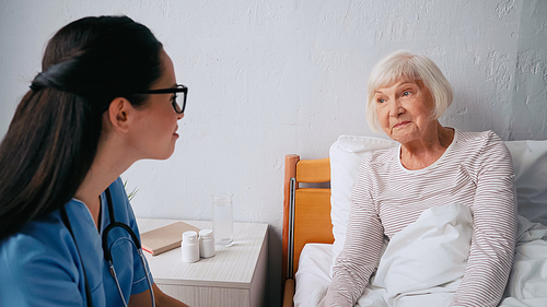 blurred nurse in eyeglasses near senior woman in clinic