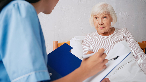 blurred nurse writing prescription near aged woman