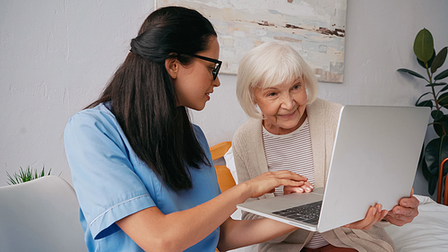 brunette geriatric nurse showing happy aged woman how to use laptop