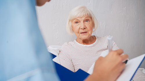 blurred geriatrician writing prescription near aged woman