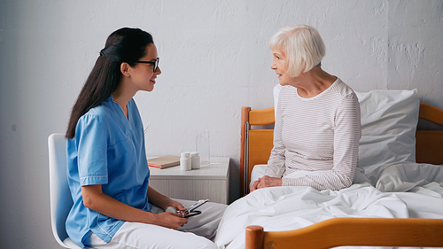 brunette nurse talking with happy aged patient and holding stethoscope