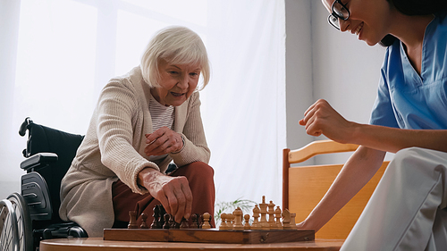 elderly woman and happy nurse playing chess in nursing home