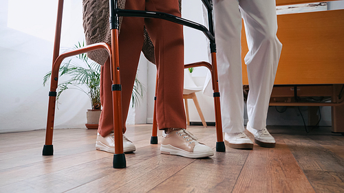 cropped view of senior woman stepping with walkers near nurse