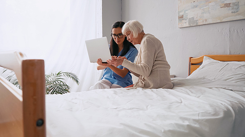 brunette geriatric nurse showing senior woman how to use laptop in nursing home