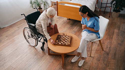 high angle view of elderly woman and nurse playing chess in nursing home