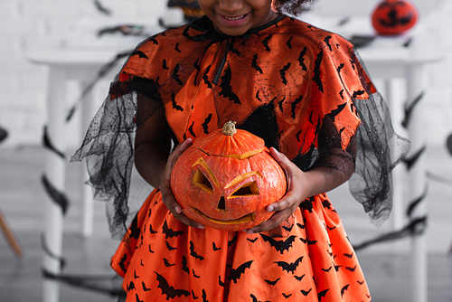 cropped view of smiling african american kid holding carved pumpkin