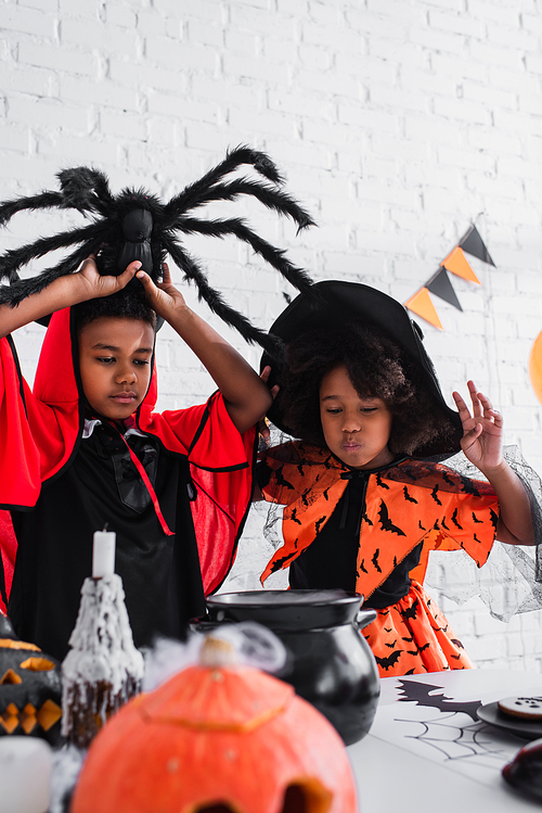african american kids in halloween costumes preparing potion in witch cauldron