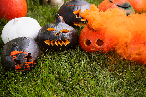 orange smoke near carved and spooky pumpkins on green lawn