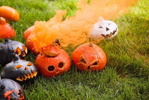 carved and spooky pumpkins with orange smoke on green lawn