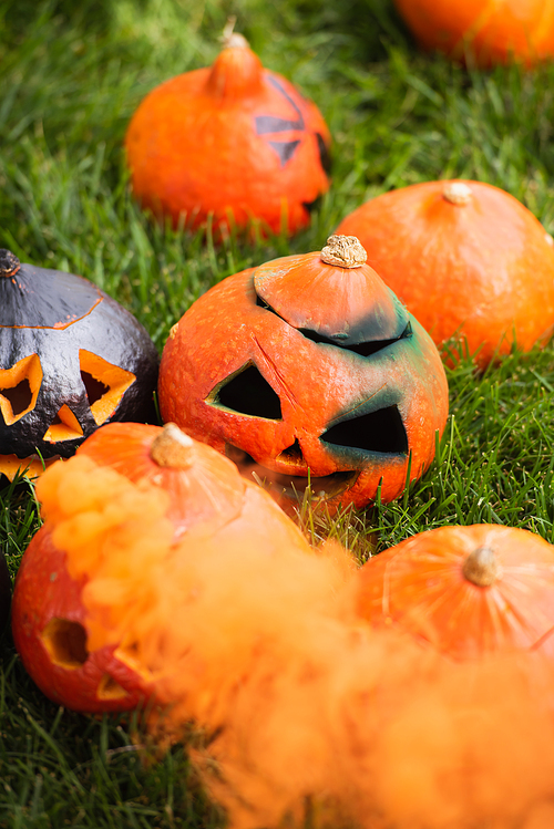 carved and scary pumpkins with orange smoke on green lawn