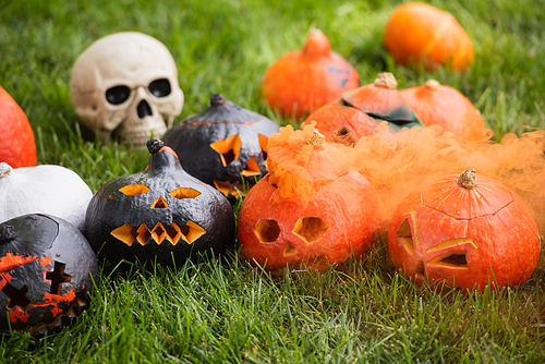 carved pumpkins with orange smoke near blurred skull on green lawn