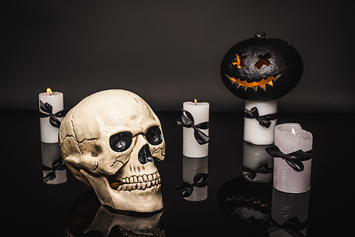 skull near burning candles and carved pumpkin on black
