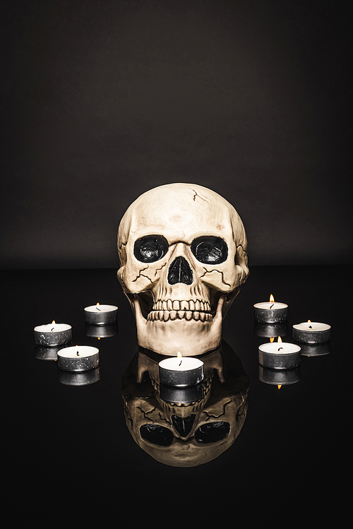 burning candles near spooky skull on black