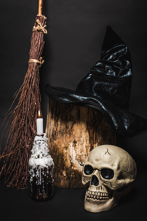 broom near skull and wooden stump with witch hat on black