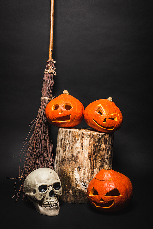 broom near skull and orange carved pumpkins on wooden stump on black