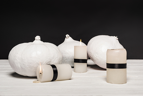 white pumpkins near burning candles isolated on black
