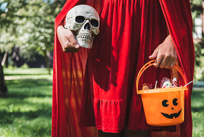 partial view of girl wearing red halloween costume and holding skull and bucket of candies