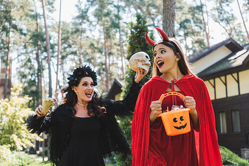 woman in vampire halloween costume screaming and scaring daughter with skull and toy hand