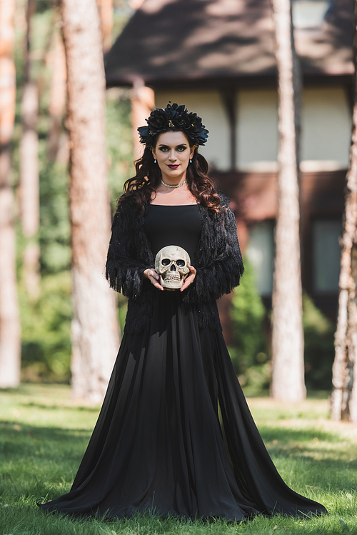 woman in black halloween costume holding creepy skull outdoors