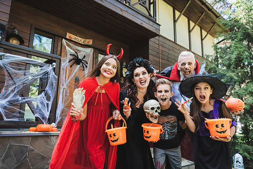 cheerful family in spooky halloween costumes grimacing at camera near house