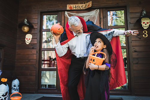 man in vampire costume scaring daughter near house with halloween decoration