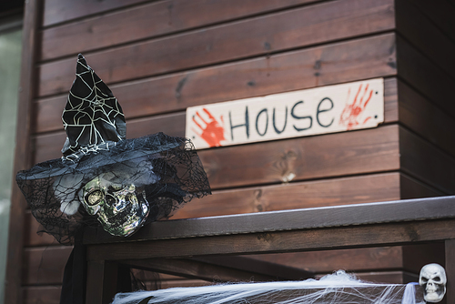 spooky skull in witch hat with black veil near blurred card with house lettering and bloody hand prints