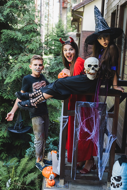 excited kids in spooky halloween costumes grimacing on cottage porch