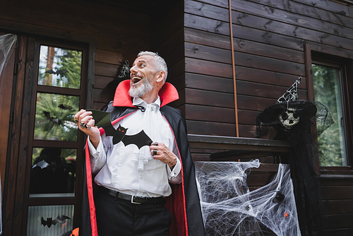 mature man in vampire halloween costume laughing on porch of decorated house