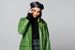 young stylish woman in beret and green leather jacket posing isolated on grey