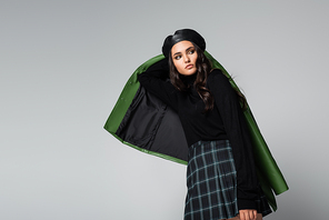 young brunette woman in plaid skirt, black beret and jacket posing isolated on grey