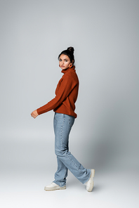 full length of pretty young woman in sweater and denim jeans posing on grey