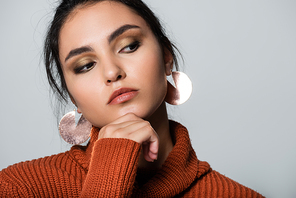 young woman in warm sweater and earrings looking away isolated on grey