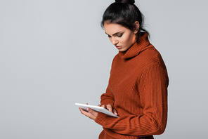 young woman in knitted sweater using digital tablet isolated on grey