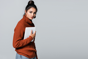 brunette young woman in knitted sweater holding digital tablet isolated on grey
