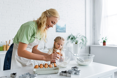 woman breaking egg into bowl while cooking with daughter in kitchen