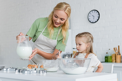 mother showing jug of milk to daughter in kitchen