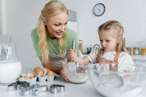 girl mixing ingredients in bowl while cooking with mom in kitchen